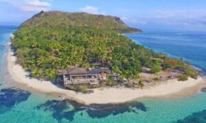 A breathtaking sunset over Vomo Island Fiji, showcasing the island's lush greenery against a backdrop of tranquil blue waters and a vibrant sky, epitomizing a luxurious and serene tropical escape